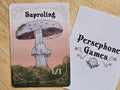 Illustrated 1/1 saproling token card featuring light gray gilled mushroom with a small line drawn face