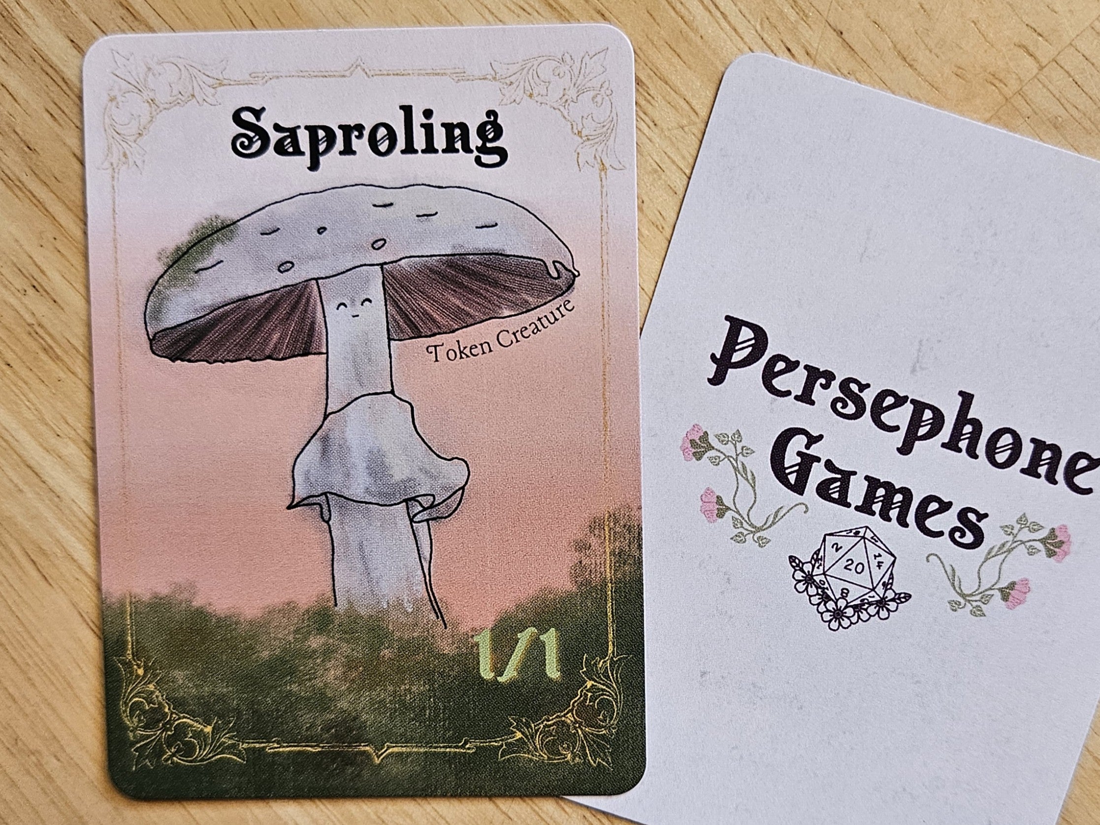Illustrated 1/1 saproling token card featuring light gray gilled mushroom with a small line drawn face