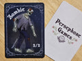 Illustrated 2/2 zombie token card featuring a bloodied, hobbling zombie glowing red eyes, torn dark blue pants and gray t-shirt that is falling apart.