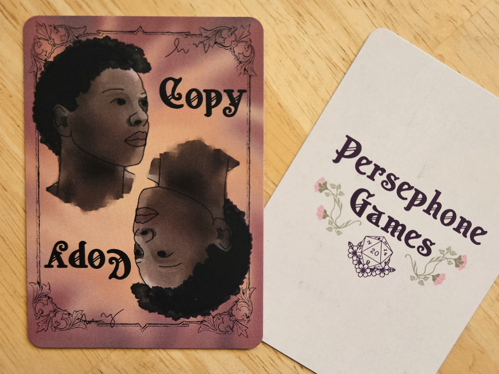 Illustrated copy token card featuring two identical faces with dark brown skin and short tightly coiled curly hair, positioned at opposite corners of the card in 180 degree rotation.