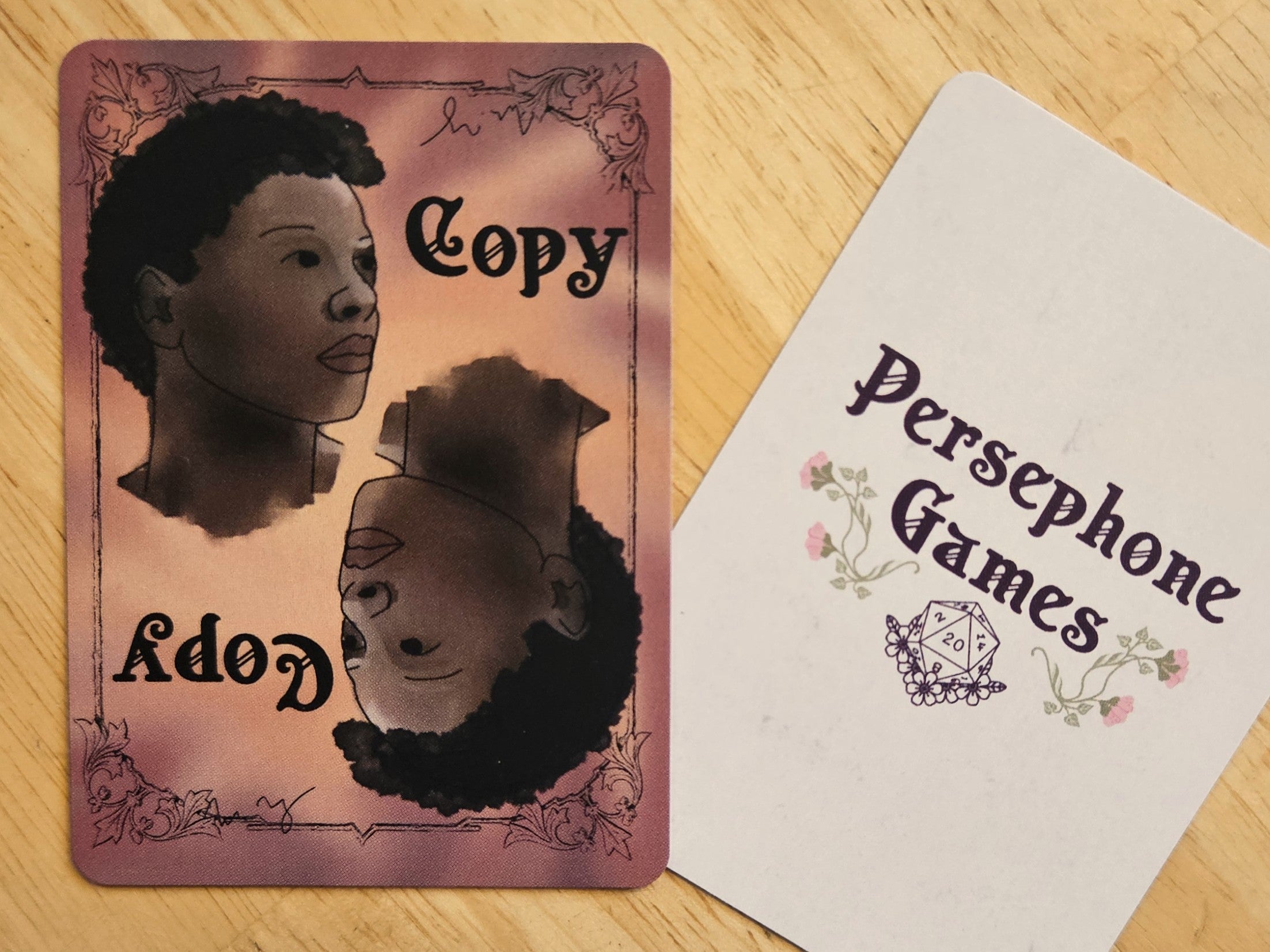 Illustrated copy token card featuring two identical faces with dark brown skin and short tightly coiled curly hair, positioned at opposite corners of the card in 180 degree rotation.